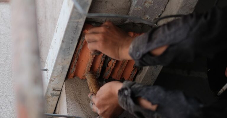Worker repairing structure with trowel, showcasing detailed craftsmanship.